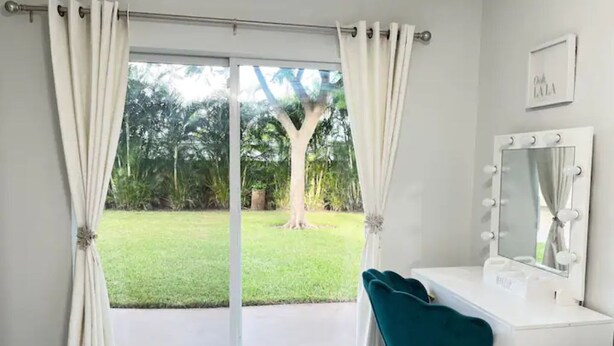 A room with a white vanity, teal chair, and a large mirror with lights. - PGA 3/2 w Backyard close to everything beach mall (West Palm Beach)
