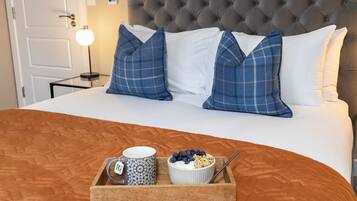 A neatly made bed with a plaid pillow set, a bedside table with a lamp, and a tray with a mug, bowl of yogurt with blueberries, and granola.