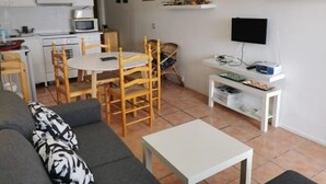 Un espacio habitable compacto con kitchenette, una zona de comedor, una sala de estar con sofá y una pequeña mesa, y un televisor montado en la pared.