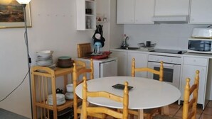 Cocina compacta con armarios blancos, un microondas y una mesa de comedor con cuatro sillas de madera.