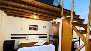 Un dormitorio con techo de madera, una cama con ropa blanca, una mesita de noche y una puerta que da a otra habitación.