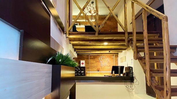 Zona de recepción de un hotel con una escalera de madera, un mostrador de recepción y un letrero que dice "CASA HOTEL".