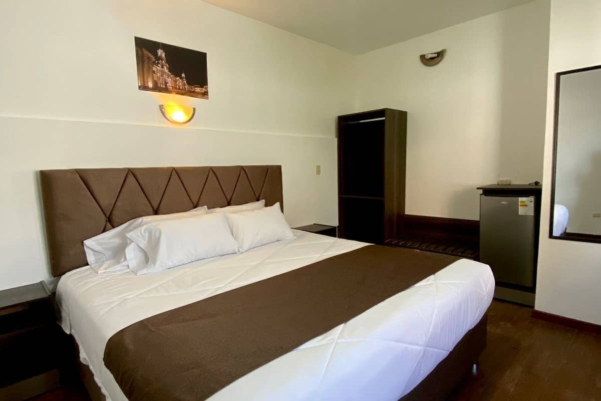 A hotel room with a large bed, a wardrobe, a mirror, and a picture on the wall.
