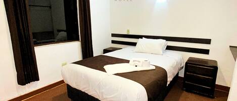 Una habitación de hotel con una cama grande, una mesita de noche y una ventana con cortinas.