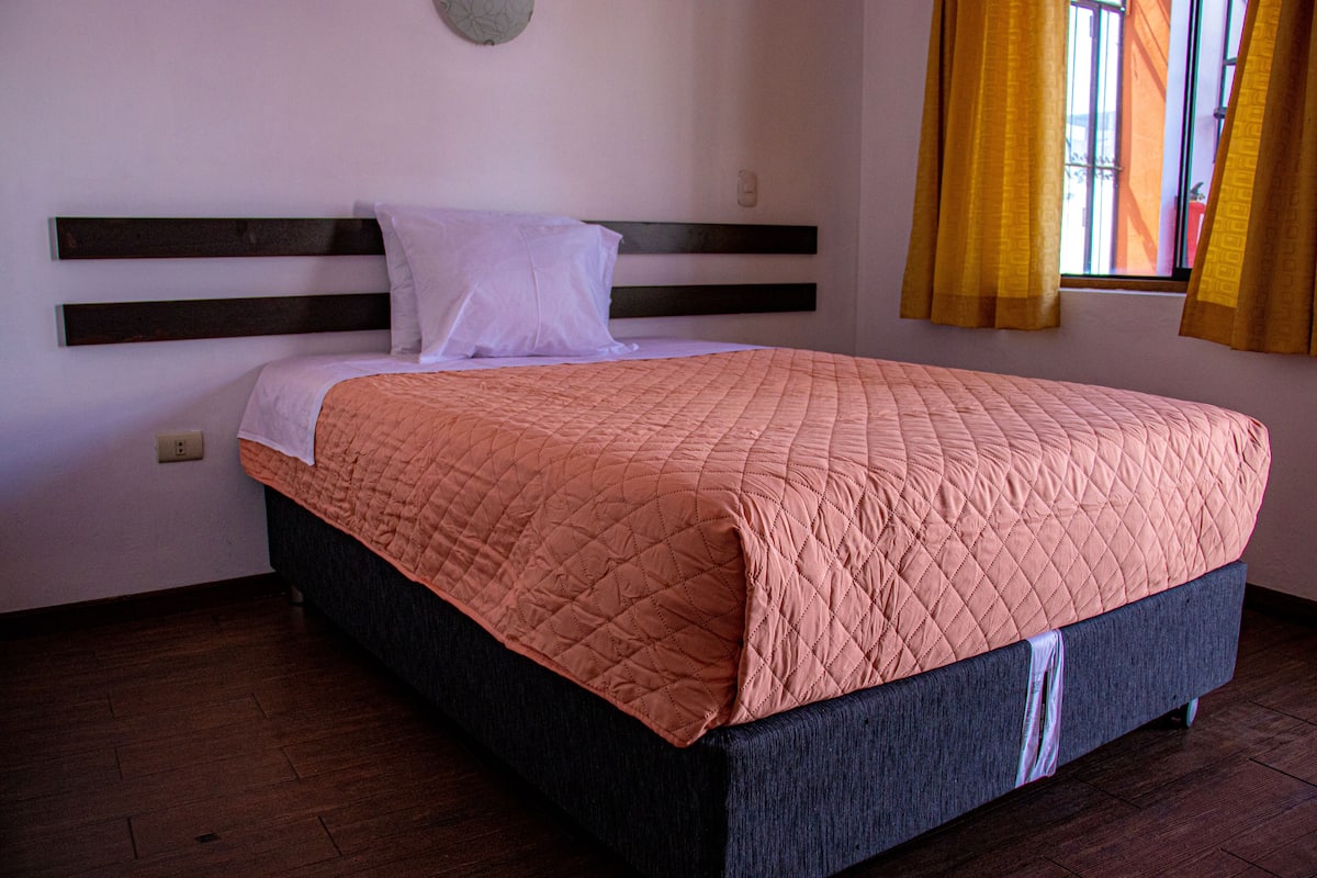 A neatly made bed with a dark headboard and a pink quilted bedspread.