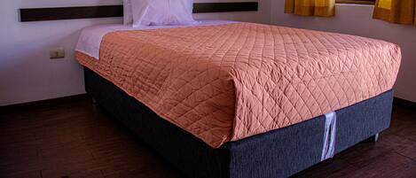 A neatly made bed with a dark headboard and a pink quilted bedspread.