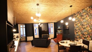 A modern kitchen with wooden flooring, a dining area with a round table and chairs, and a ceiling with exposed beams and pendant lighting. - Duplex spa (Bagnères-de-Bigorre)