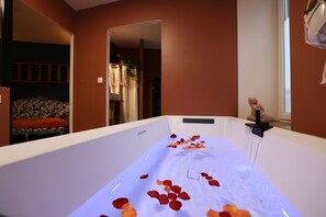 A bathtub with rose petals, a small statue, and a plant. - Duplex spa (Bagnères-de-Bigorre)