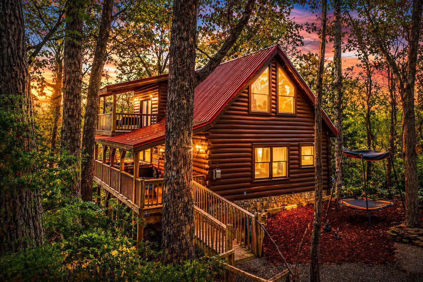 Eine Blockhütte mit Balkon und Trampolin in einem Wald.