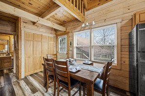 Un interior de madera con una mesa de comedor preparada para cuatro, un refrigerador y una ventana con persianas.
