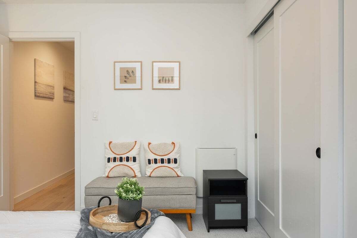 Une chambre à coucher avec un lit, une table de chevet, une petite table sur laquelle est posée une plante, et deux tableaux encadrés accrochés au mur.