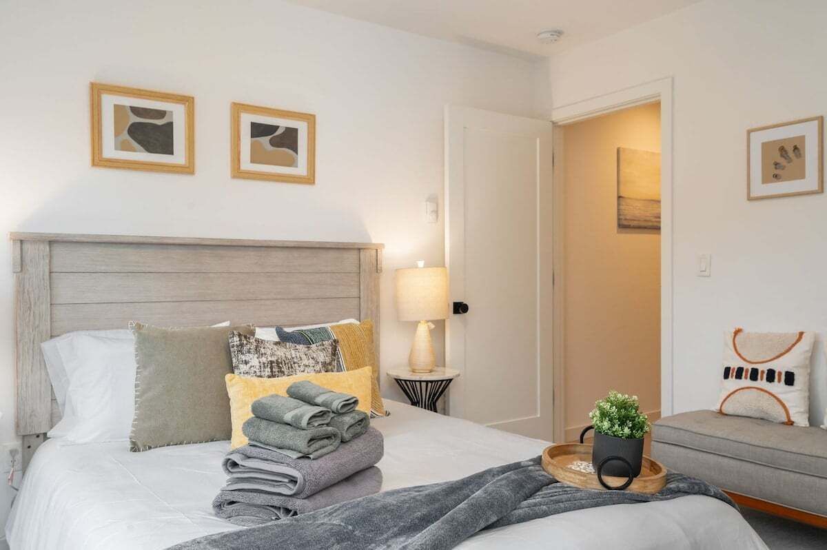 Ein ordentlich bezogenes Bett mit Handtüchern, einer Nachttischlampe und einem kleinen Tisch mit einer Pflanze.