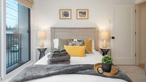 A hotel room with a bed, two bedside lamps, a window with a view, and a door. - Perch - Sand Point Haven: Spacious 3BR w Parking|UW & Children's hospital (Seattle)