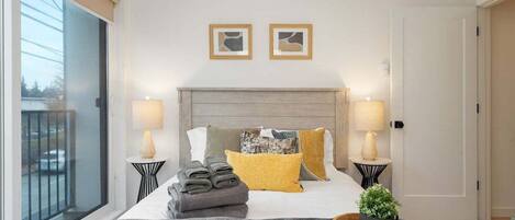 A hotel room with a bed, two bedside lamps, a window with a view, and a door.