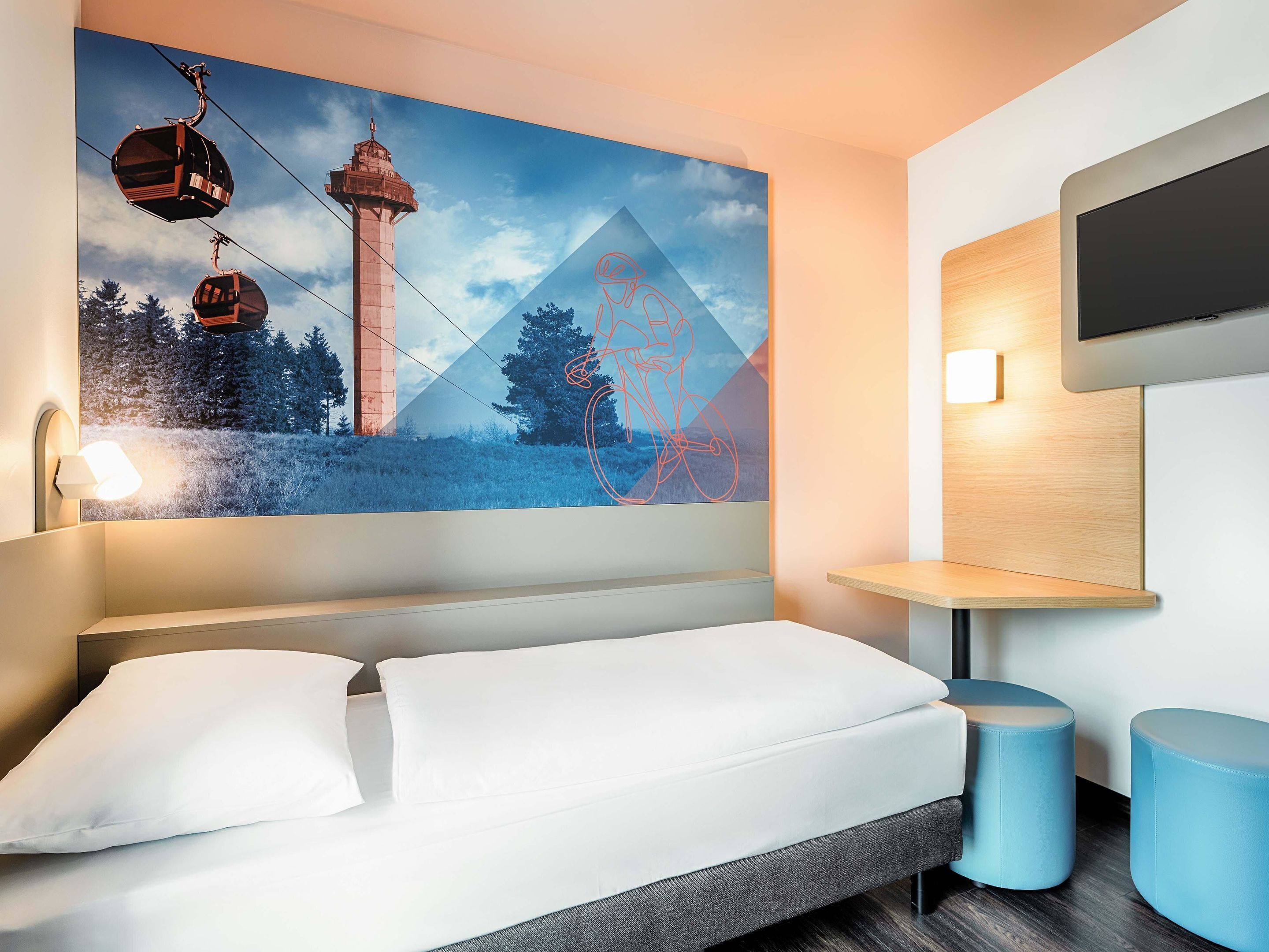 A modern hotel room with a large bed, a mounted TV, and a wall-mounted shelf.