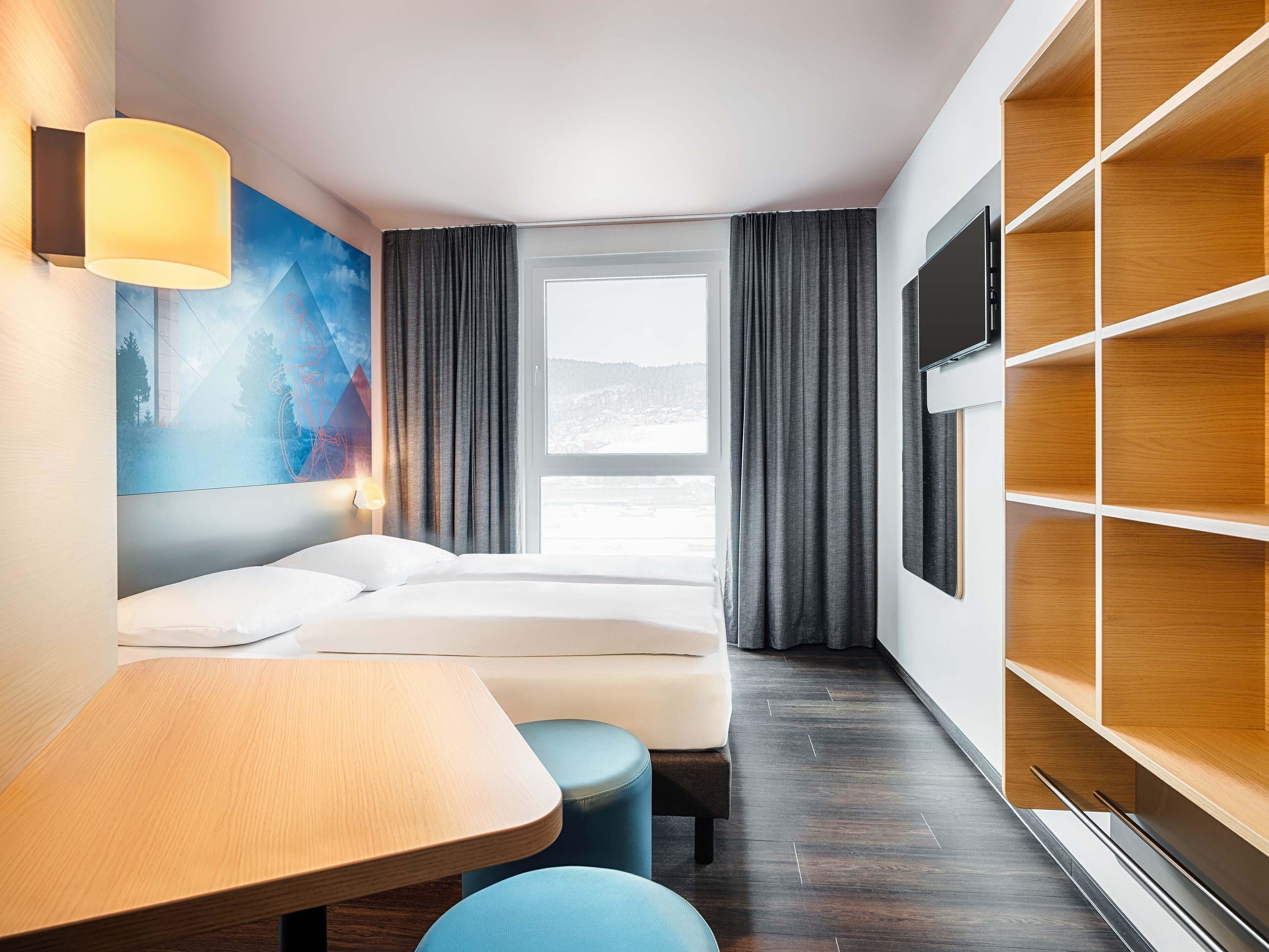 Een hotelkamer met een bed, een bureau, een televisie en een groot raam met gordijnen.