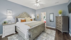 Un dormitorio con cama, mesitas de noche, cómoda, ventilador de techo y una puerta.