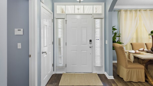 Un pasillo con una puerta blanca, una lámpara y un comedor con mesa y sillas.