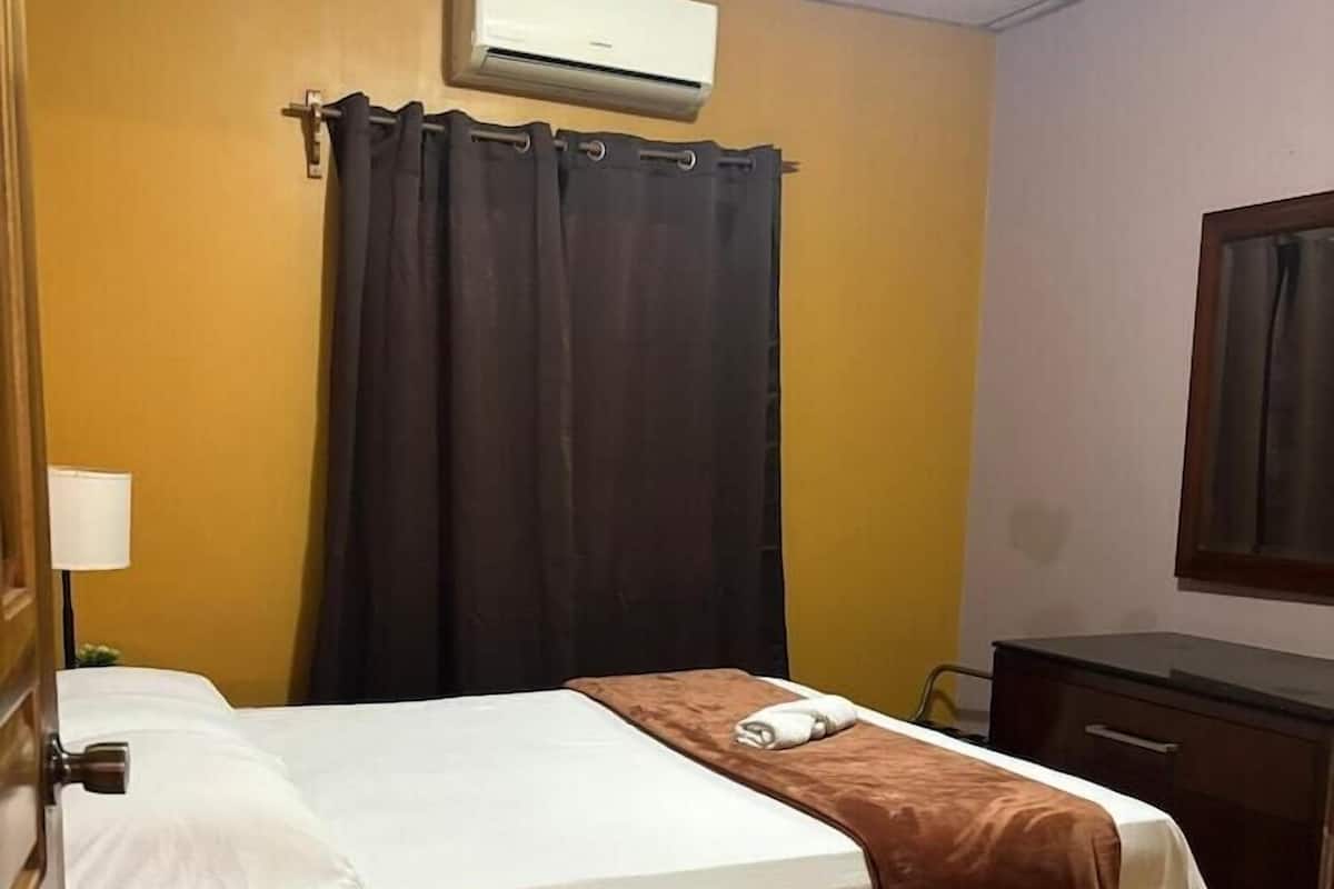 A hotel room with a bed, a desk, an air conditioner, and a curtain.