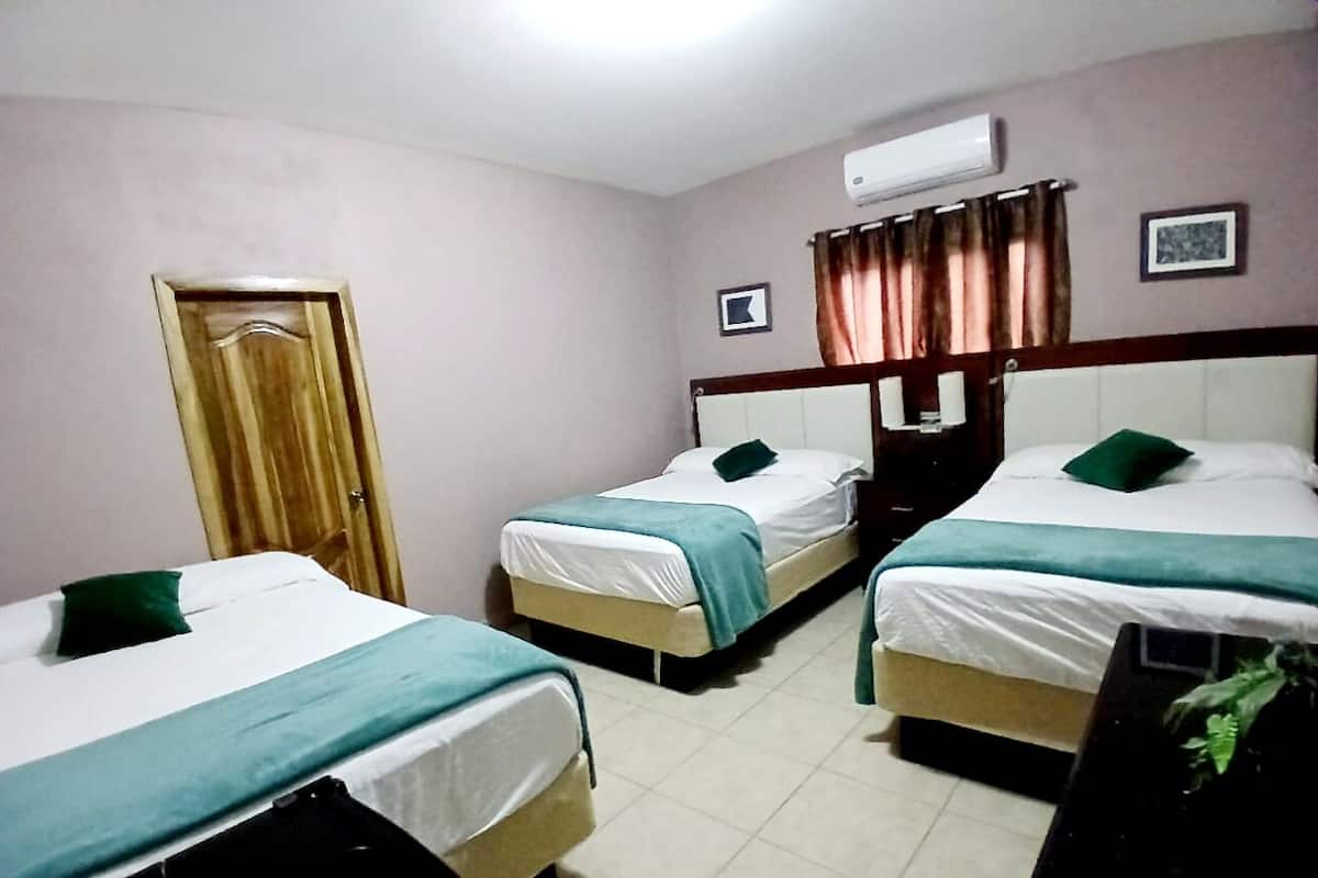 A hotel room with three single beds, a wooden door, an air conditioning unit, and a small framed picture on the wall.