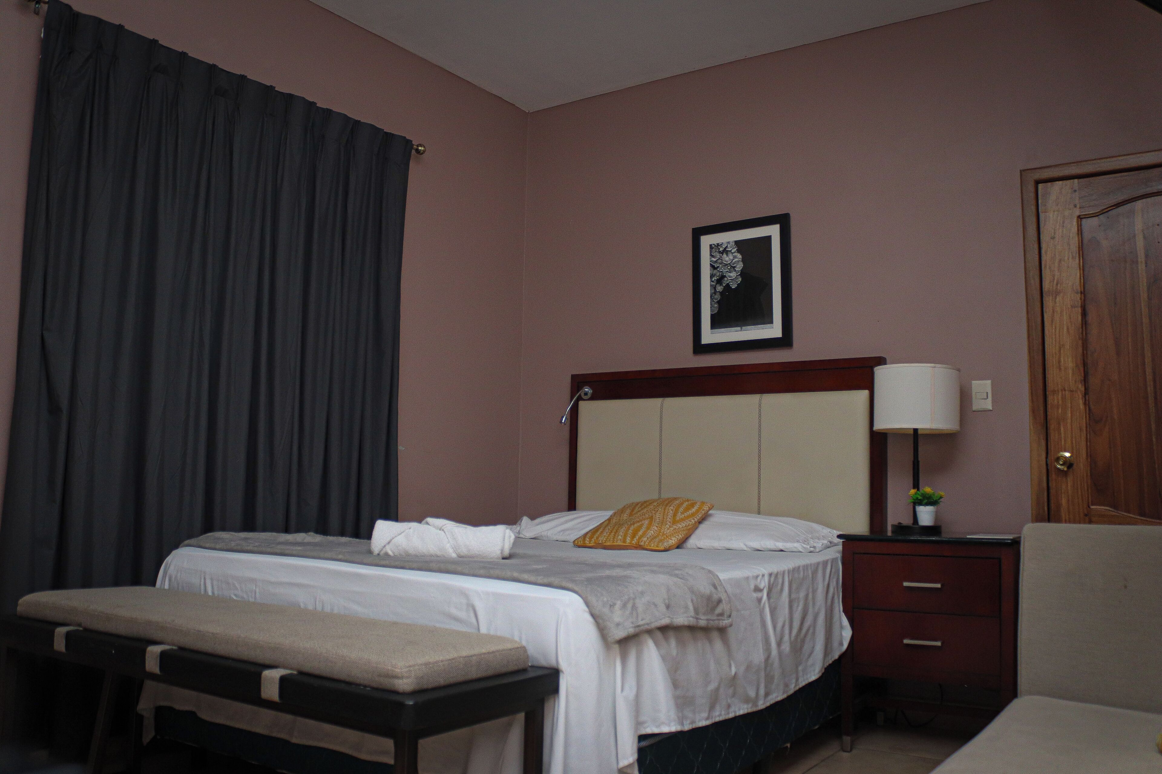 A hotel room with a bed, bedside table, lamp, and a door.