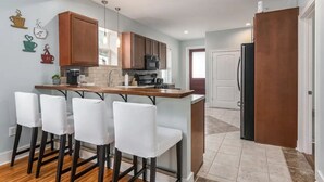 A modern kitchen with a central island, bar stools, wooden cabinets, and a refrigerator. - Chestnut Street Charmer-Walk to Louisville! (Jeffersonville)