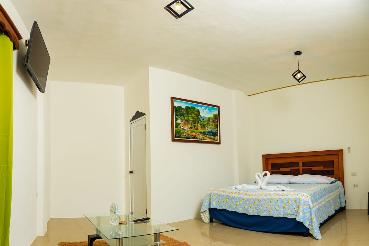Ein Schlafzimmer mit einem Bett, einem Glastisch, einem Gemälde und einer Deckenleuchte.
