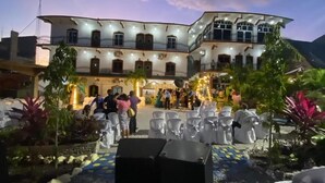 A large, multi-story building with a curved facade, outdoor seating area with white chairs, and a well-lit entrance. - Hotel y Restaurante Las Adas y Estrellas (Melchor de Mencos)