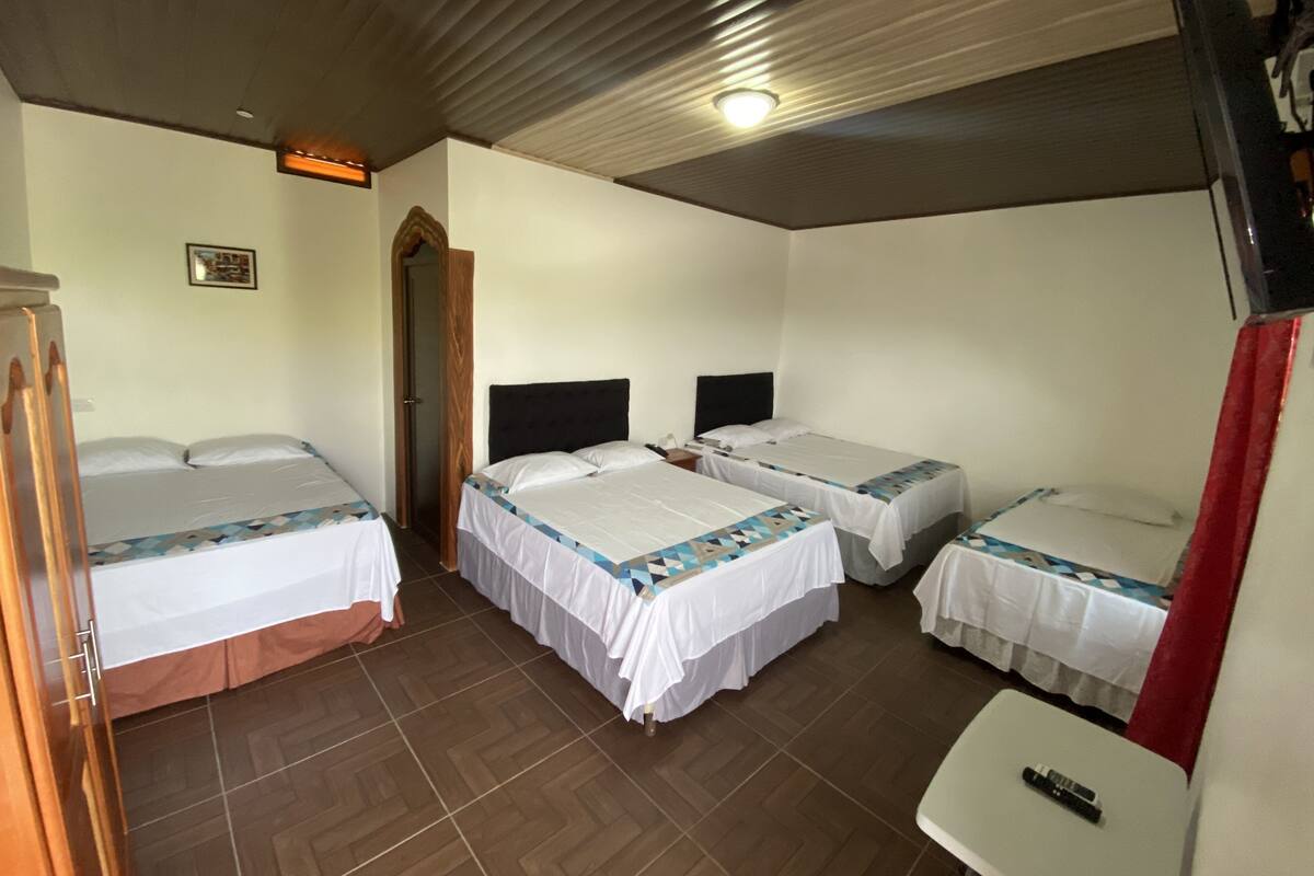 Ein Hotelzimmer mit drei Einzelbetten, einem kleinen Tisch und einer Holztür.
