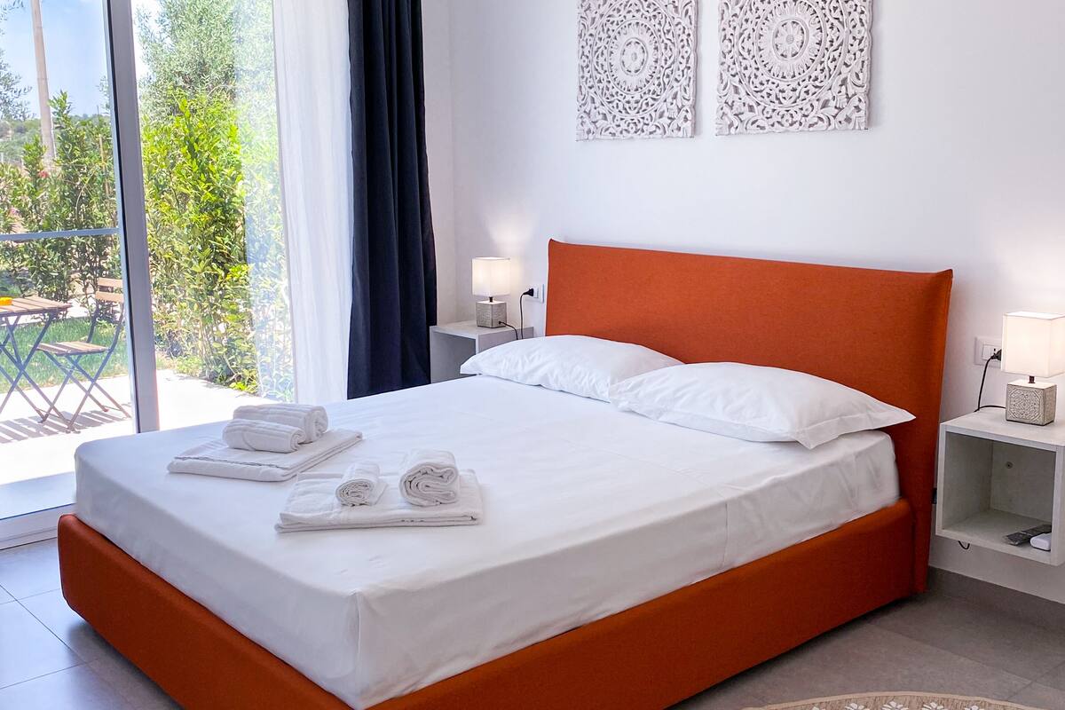 A hotel room with a bed, two bedside lamps, a nightstand, and a view of the outdoors.