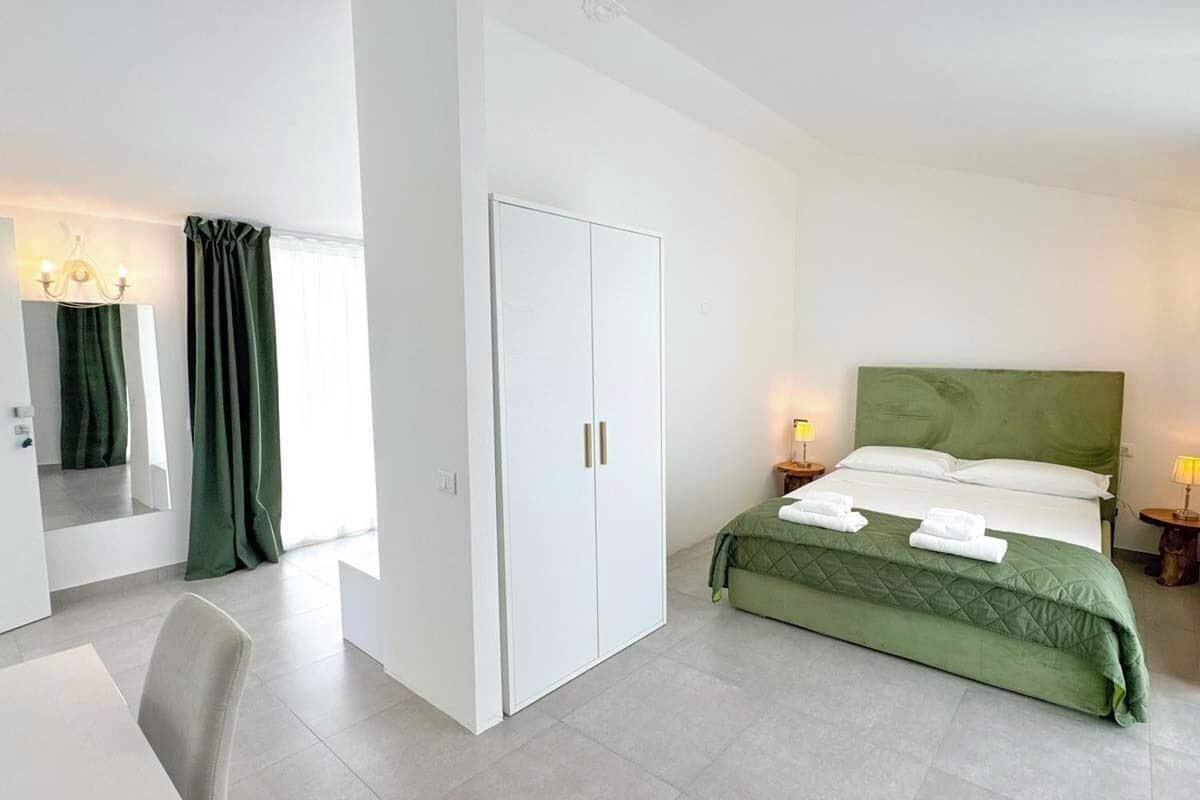 A modern hotel room with a bed, a wardrobe, a desk, and a chair.