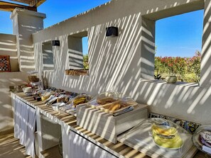 Montaje de desayuno buffet con diversas opciones de comida y recipientes, un rebozo de azulejos y vistas a un jardín con flores.