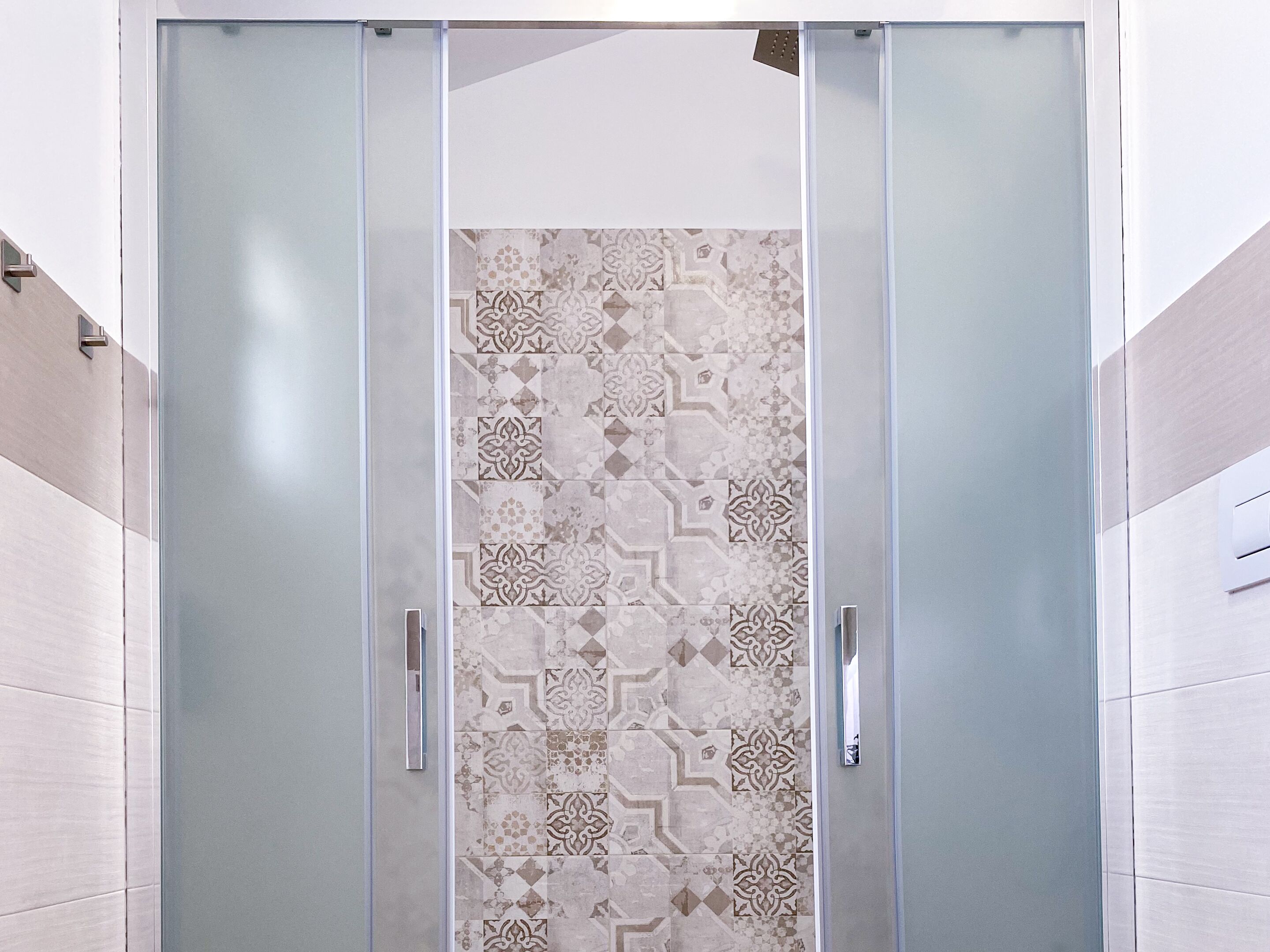 A modern bathroom with a glass shower enclosure, patterned tiles, and a minimalist design.