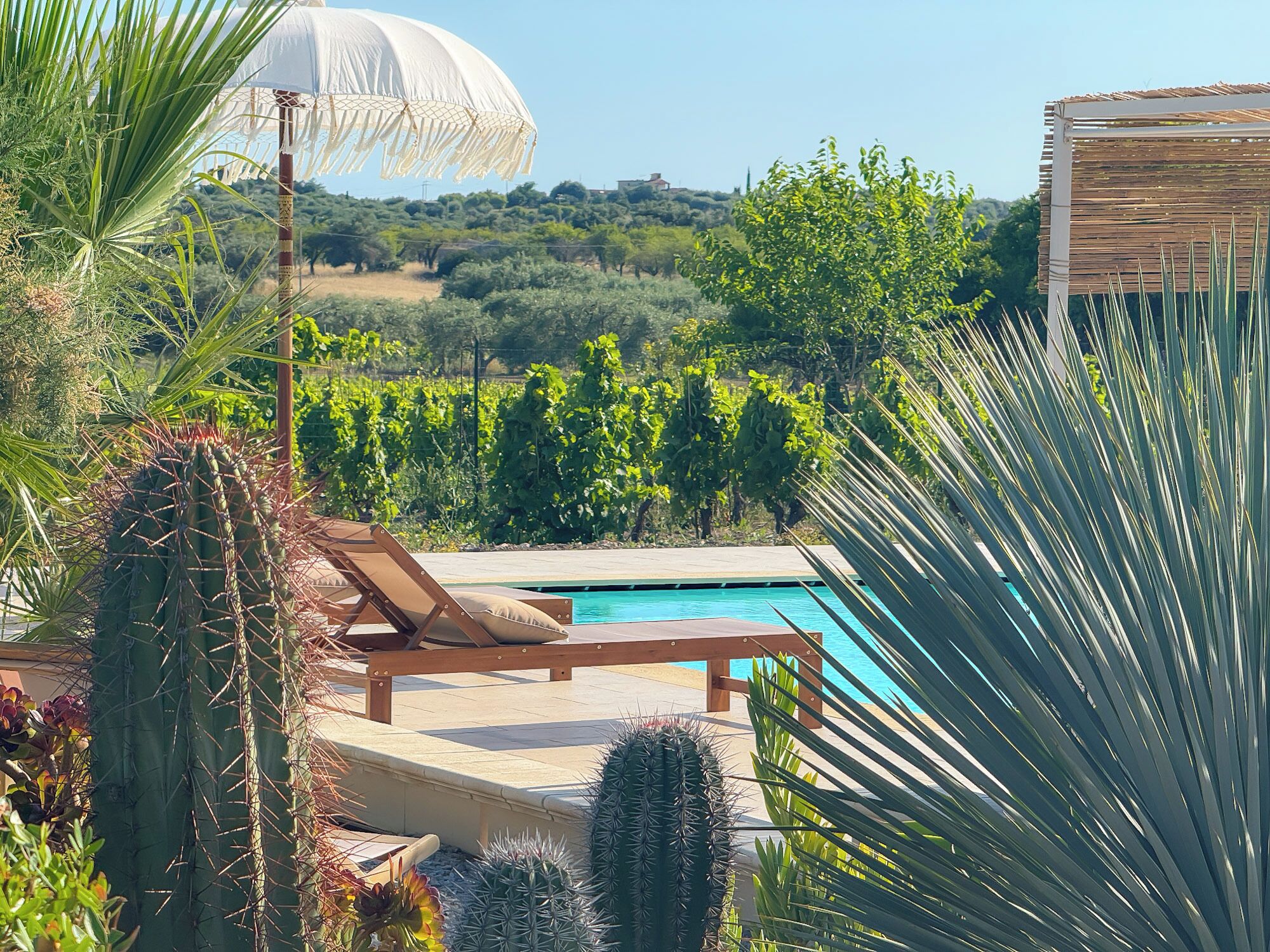 A pool area with a wooden lounge chair and a white umbrella.