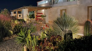 A modern house with a covered patio, a red outdoor seating area, and a variety of plants and cacti. - Dimora Calauriia - Adults Only (Noto)