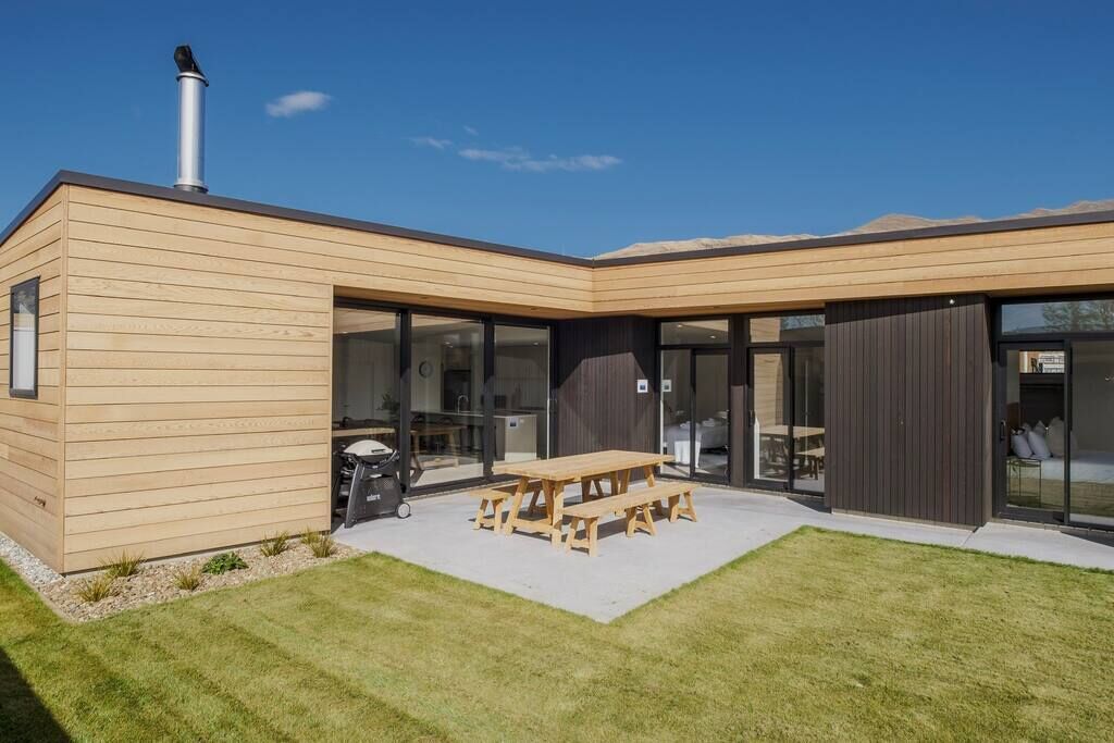Ein modernes Haus mit Holzfassade, großen Schiebegläsern und einer Terrasse mit Holztisch und Bänken.
