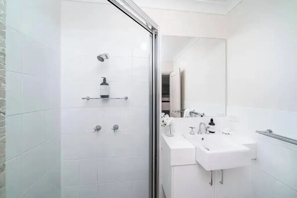 A modern bathroom with a glass shower enclosure, a white sink, and a mirror.