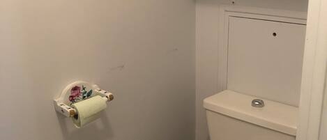 A small bathroom with a toilet, a toilet paper holder, and a shelf above the toilet.