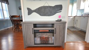 A living room with a fireplace, wooden flooring, a dining area with chairs, and a kitchen in the background. - Walking distance to shopping, restaurants, entertainment, and the Chesapeake Bay (Rock Hall)