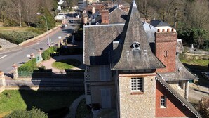 Un edificio histórico con una torre destacada y muros de piedra, rodeado por un pequeño pueblo con una carretera y vegetación.