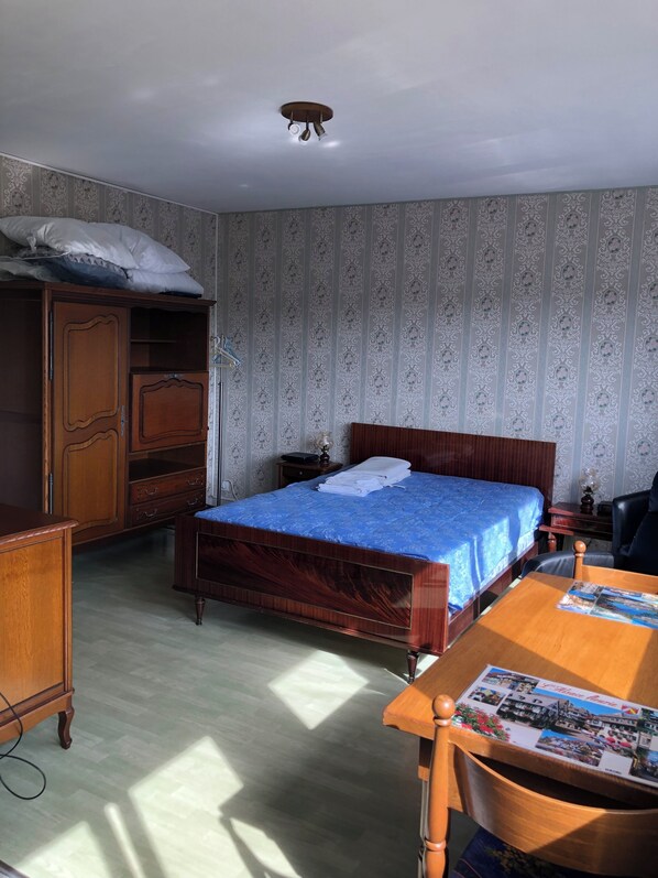 A bedroom with a wooden bed, a wooden desk, a wardrobe, and a ceiling light fixture.