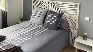 A bedroom with a bed, grey bedding, a white headboard, and a small bedside table.