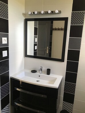 Un baño con un lavamanos blanco, un mueble de tocador negro, un espejo con luces arriba y azulejos estampados.