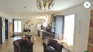 A modern living room with a dining table, two armchairs, and a kitchen in the background.