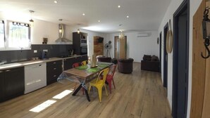 A modern kitchen with a dining area, wooden flooring, and a view of the living room.