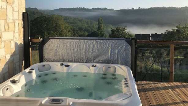 A hot tub on a wooden deck with a view of a forested hill and mist.