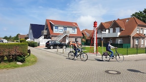 Una strada residenziale con case, un palo del telefono rosso e due ciclisti.