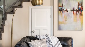 Una stanza con un divano in pelle nera, una porta bianca, un quadro astratto dai colori vivaci e una lampada da terra in ottone.