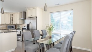Una cucina moderna con mobili bianchi, elettrodomestici in acciaio inox e un tavolo da pranzo in vetro con sedie grigie.