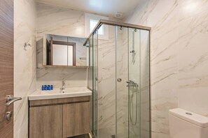 Een moderne badkamer met een douche met glazen wand, een houten wastafelmeubel en een wand betegeld met marmer.